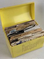 Yellow plastic recipe box open showing tabs and numerous recipe cards and clippings