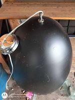 Black matte metal dome pendant on its side showing chrome canopy and electrical cord