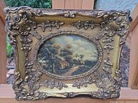 Front view of framed painting showing ornate gilt frame and oval landscape