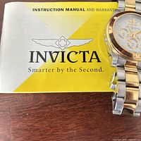 Invicta instruction manual beside partial view of two-tone wristwatch
