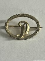 Front view of gold-tone oval brooch with raised letter D and floral border