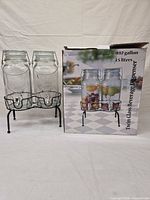 Two glass beverage dispensers on black metal stand beside original box