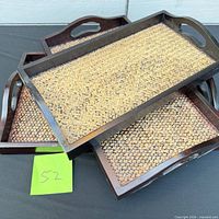Three stacked wood trays showing woven rattan surfaces and cut-out handles