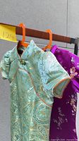 Front view of green/teal brocade qipao with orange piping and frog closures