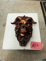 Front view of copper-tone horned skull door knocker on packing foam