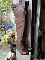 Full view of the pair of brown knee-high boots hanging, showing color, height, toe shape