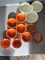 Ten orange ramekins and three white bowls laid out on sofa