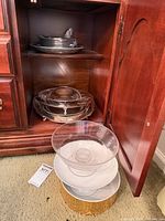 Pewter servers on upper shelf, silver-plated chafing dish on lower shelf, three bowls on floor