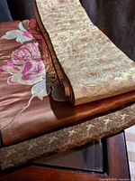 Three folded silk textile pieces showing embroidery and woven patterns