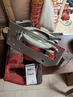 Underside view of circular saw showing blade, part of reciprocating saw handle and battery