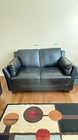 Front view of black faux leather loveseat showing overall design and both arm cushions