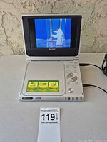 Player open, screen on displaying video, power adapter visible