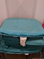 Stack of four teal outdoor seat cushions with tags and corner ties