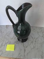 full view of glazed ceramic pitcher standing on base