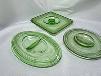Two oval and one square green uranium glass lids displayed on white backdrop