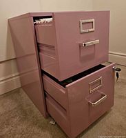 Oblique front view with both drawers partially open showing pink metal cabinet and hanging file rails