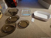 Group shot of six glass baking dishes: four smoked amber, one clear square, one white rectangular with blue floral