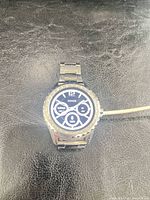 Front view of powered-on Guess smartwatch with metal bracelet and charging cable