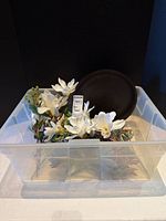 Clear bin containing dark charger and assorted faux botanicals