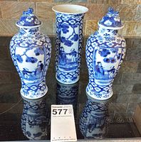 Three blue and white porcelain pieces on stovetop: two lidded ginger jars and one cylindrical vase