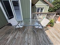 Full view of square glass top table and two sling chairs on deck