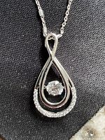 Close-up of pendant showing teardrop shape, central floating stone, cubic zirconia arc