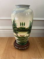 Full view of ceramic vase on stand showing painted landscape