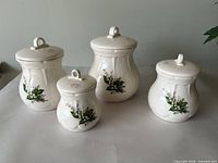 Four cream/off-white Grand River Pottery lidded ceramic pieces with lily-of-the-valley floral decals shown together