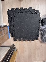 Stack of black rubber interlocking tiles showing top surface and speckled pattern
