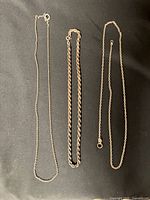 Three silver necklaces laid flat: rope chain centered, cable chains left and right.