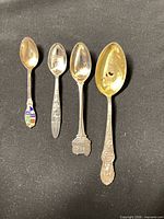 Four sterling silver souvenir spoons on black background showing relative sizes, enamel crest and gilt bowl visible