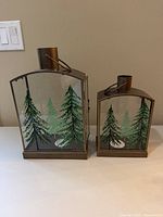 Two bronze metal framed lanterns with tree-painted glass panels, large and small sizes