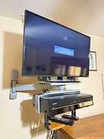 Front view of TV on wall mount with VCR/DVD combo and remotes on shelf