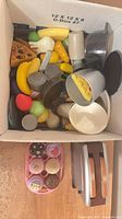 Open box showing mixed plastic food items, pots, pans, toaster and dessert tray