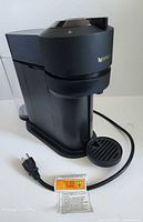 Front three-quarter view of Nespresso Vertuo Next with water tank, drip tray and power cord visible