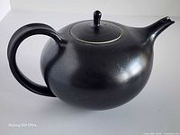 Left side view of matte black pottery teapot with handle, spout and lid