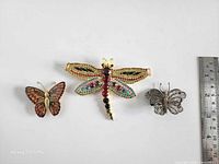 Front view of three brooches showing motifs and rhinestones