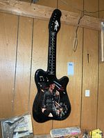 Front view of guitar-shaped Elvis wall clock hung on wood paneling