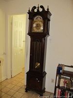 Full view of Ethan Allen grandfather clock standing tall against wall showing entire wooden case and height.