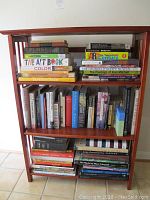 Full view of one of three reddish-brown wooden bookcases filled with books on various subjects including art, fiction, and history.