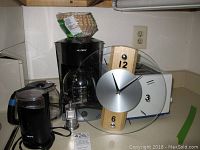 Wide view of all items in the lot including Mr Coffee coffeemaker, Krups grinder, pepper mill, toaster, wall clock, and coffee filters.