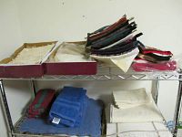 Various pot holders stacked on a shelf with folded linens and lace nearby.