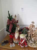 Tabletop display of Christmas decor including Royal Dux figurine, Heartwood Creek Santas, small Christmas trees with lights, ornaments, and wreaths.