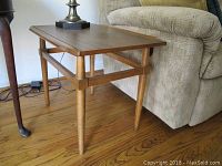 Side view of a mid century modern wooden end table with tapered legs and horizontal support near the bottom, showing wood grain and finish condition.