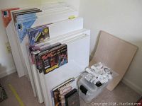 Multiple pre-stretched canvases leaning against wall with plastic bin and books visible