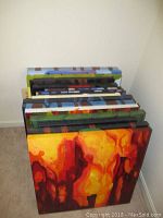 Multiple canvas art paintings stacked in a corner showing varied vibrant colors with abstract themes.
