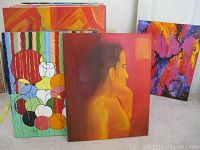 Stacked canvases showing abstract and oil paintings with a mix of geometric and figurative styles, warm color palettes including reds and oranges, varying sizes mostly between 16x20 and 18x24 inches.