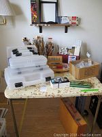 Photo showing plastic storage boxes, paint brushes in clear holders, small art tools, and a wooden box.