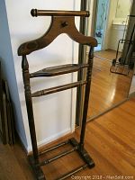 Wood valet stand made of dark stained wood with visible wear and scratches in room next to mirrored closet door