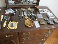 Full overview of watches, jewelry, belt buckles, small floral dish, carved plastic set, and trinket box arranged on a wooden dresser.